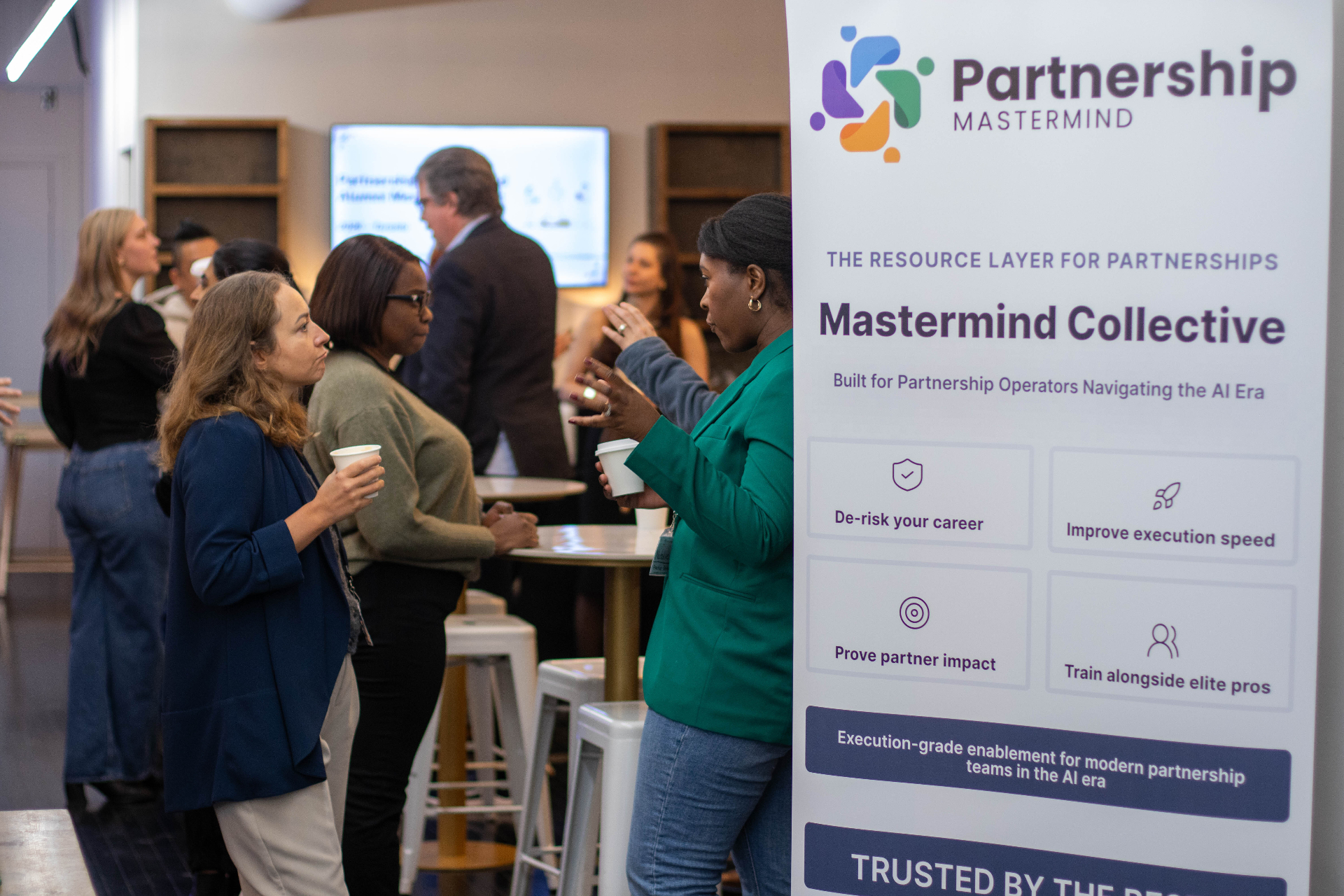 Members networking near the Partnership Mastermind Collective banner